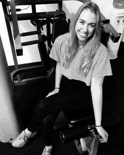 Evie Lawrie smiling, sitting on a leg machine in the gym.